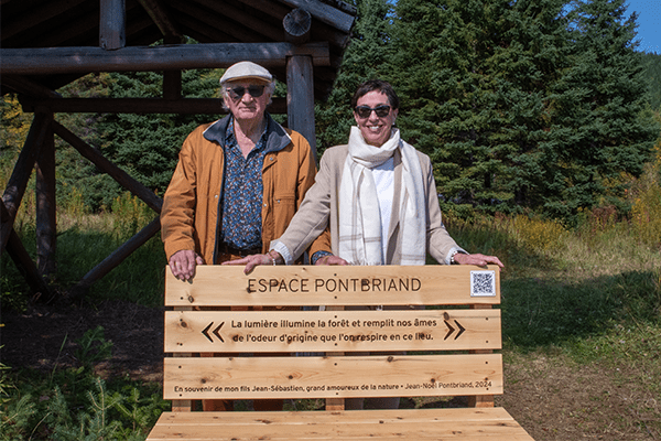 Deux personnes dehors sourient derrière un banc de bois